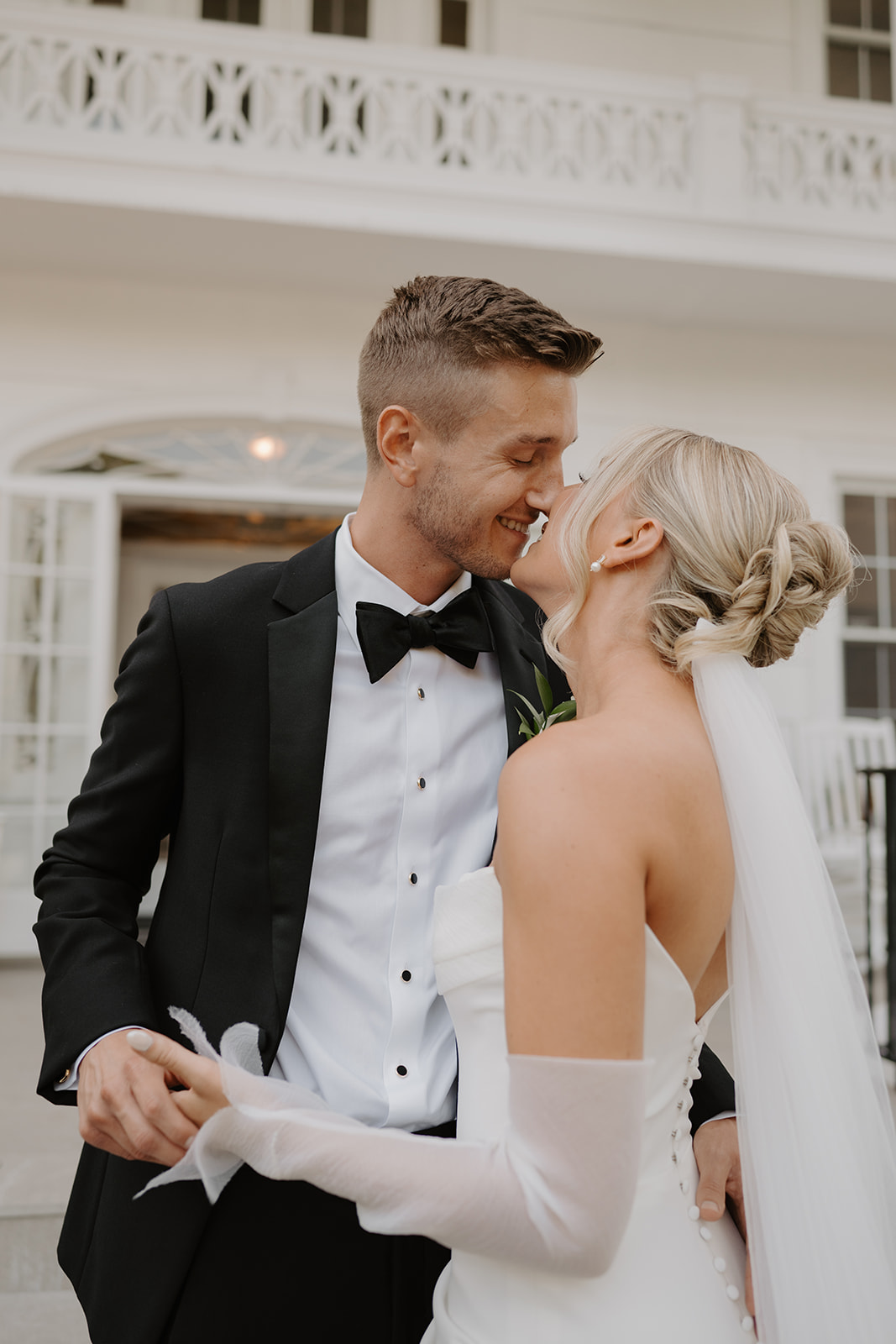 Groom rubs noses lovingly with the bride as they share a sweet smile on the outdoor terrace.